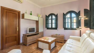 Un salon moderne avec une porte en bois, un téléviseur, un canapé blanc, une table basse en bois et une fenêtre à sommet en arc de cercle.