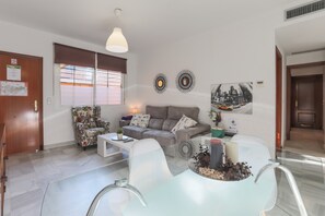 En moderne stue med sofa, lænestol, sofabord og et spisebord i glas.