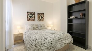 Une chambre à coucher comprenant un lit, deux horloges murales, une table de chevet, une lampe, une bibliothèque et une fenêtre avec des rideaux.