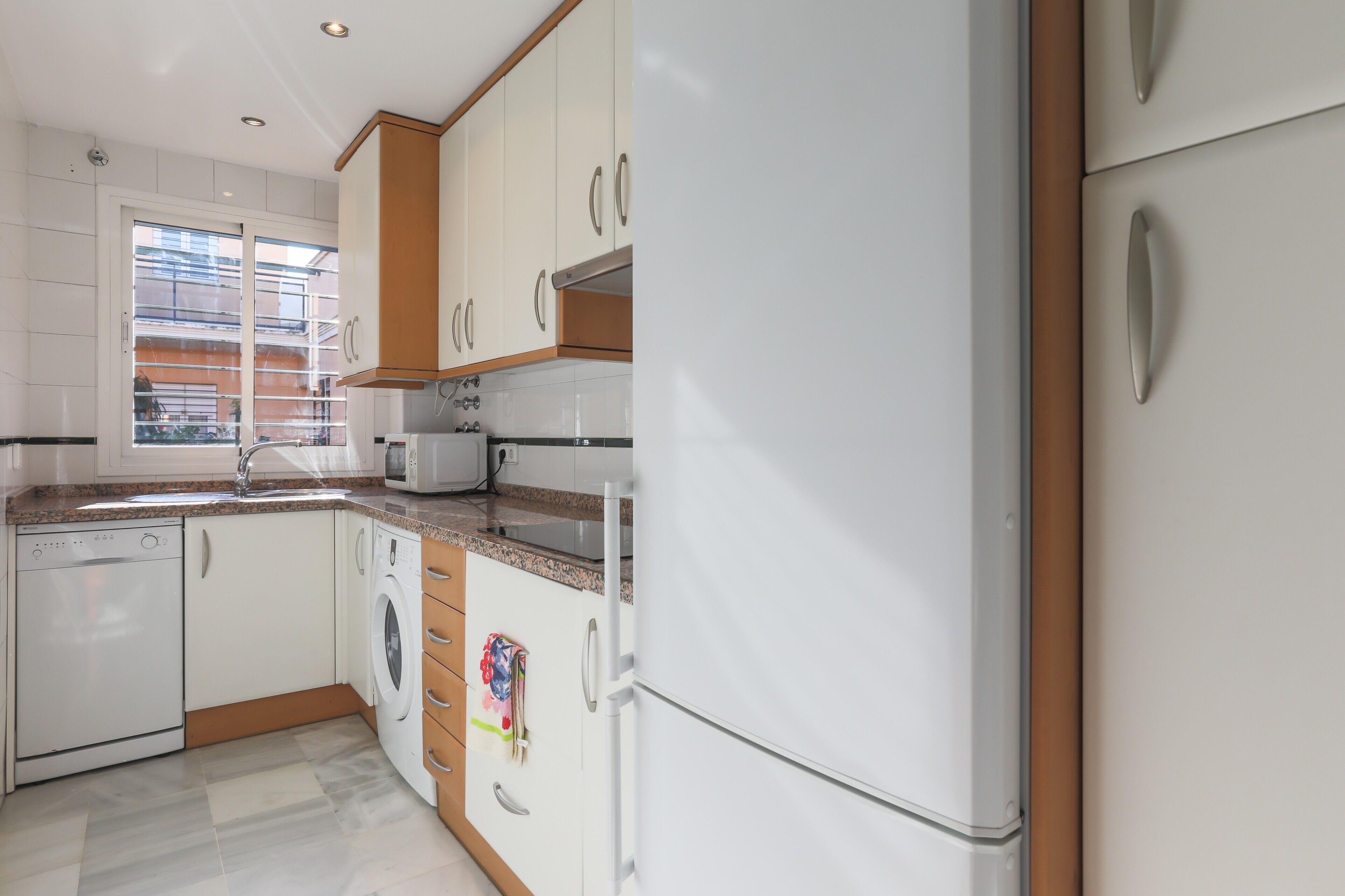 A modern kitchen with white cabinets, a dishwasher, a washing machine, and a refrigerator.