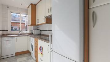 A modern kitchen with white cabinets, a dishwasher, a washing machine, and a refrigerator.