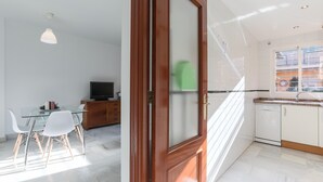 Une cuisine moderne avec des meubles blancs, un lave-vaisselle et une fenêtre équipée de stores.