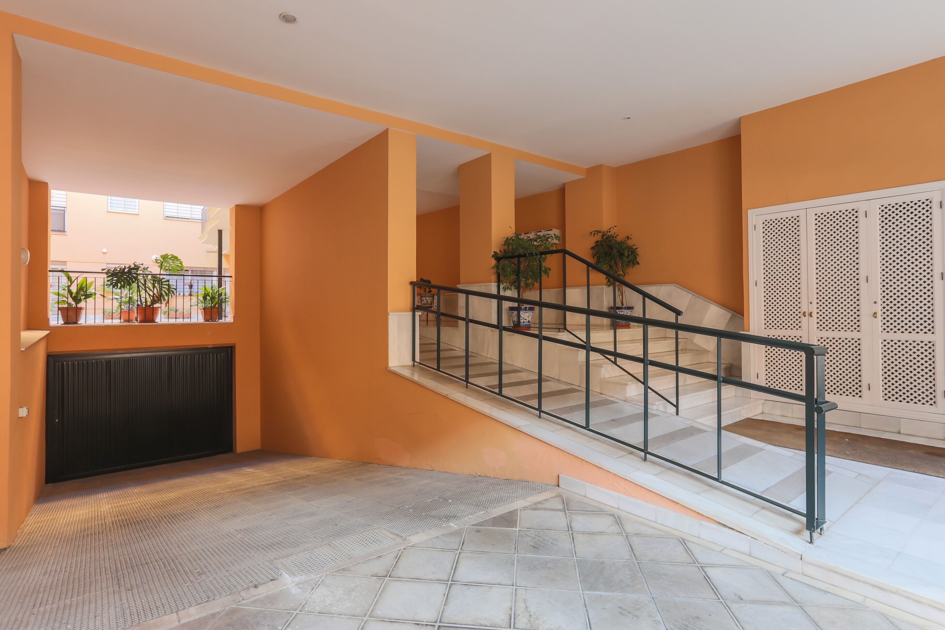 Un interior moderno con una escalera, plantas en macetas y vistas al exterior.