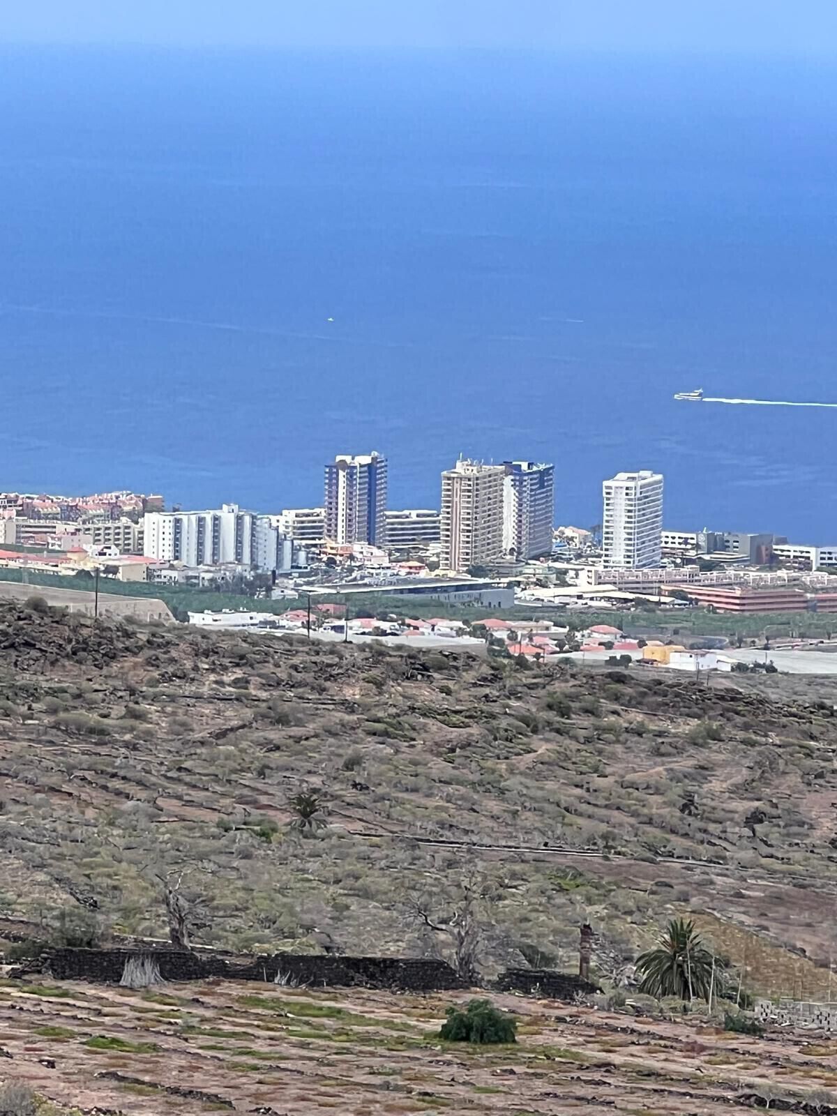 A coastal cityscape with high-rise buildings, a clear blue sky, and a distant airplane.