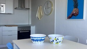 A modern kitchen with white cabinets, a stainless steel range hood, a wall-mounted clock, and two bowls on the counter. - Tartaga Penthouse (Adeje)