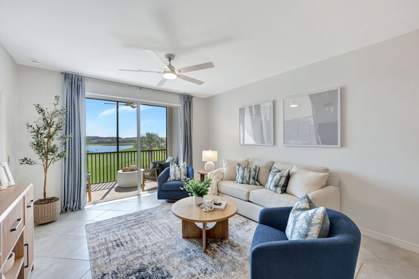 A modern living room with a large sliding glass door leading to a balcony with a view of a lake and greenery.