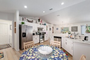 A modern kitchen with white cabinets, stainless steel appliances, and a round dining table with a floral tablecloth. - Villa Willow Wood 3-Bedroom Home Private Pool (Inverness)