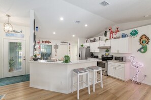 A modern kitchen with white cabinetry, a central island with bar stools, and decorative wall art. - Villa Willow Wood 3-Bedroom Home Private Pool (Inverness)