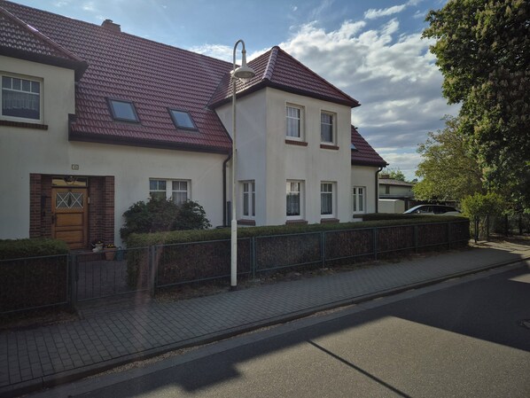 Une maison à deux étages, avec un toit recouvert de tuiles rouges, une entrée en briques et une allée pavée.