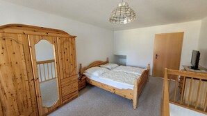 Un dormitorio con un armario de madera, una cama, un escritorio con una computadora y una lámpara colgante.