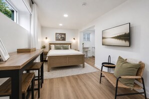 Een slaapkamer met een bed, nachtkastjes, een bureau, een stoel, een lijst met foto en een schilderij aan de muur.