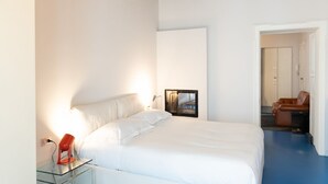 A modern hotel room with a large bed, a glass side table with a red lamp, a wall-mounted TV, and a separate seating area with a brown leather chair. - Stunning two-bedroom flat in the centre of Milan (Milano)
