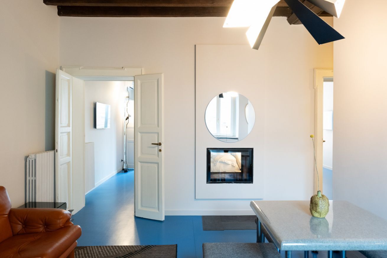 A modern living room with a blue floor, a brown leather sofa, a small table, and a round mirror on the wall.
