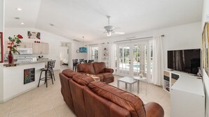 Una sala de estar moderna con un sofá de cuero marrón, un comedor con mesa blanca y una cocina con armarios blancos.
