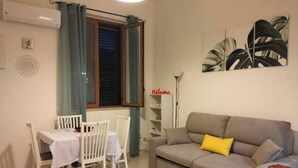 A living room with a grey sofa, a dining table with white chairs, and a window with curtains. - Saraceno Holiday Home Piazza Indipendenza Palermo (Palermo)