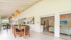 A spacious dining area with a wooden table and chairs, a kitchen in the background, and a view of the outdoors. - Granada (Le Diamant)