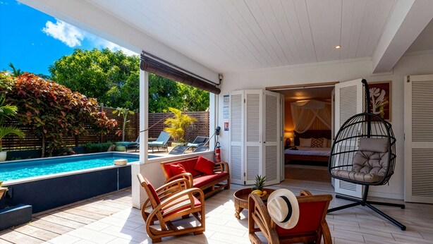 A covered outdoor area with a pool, wooden furniture, and a hanging chair. - Granada (Le Diamant)