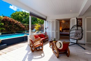 A covered outdoor area with a pool, wooden furniture, and a hanging chair. - Granada (Le Diamant)