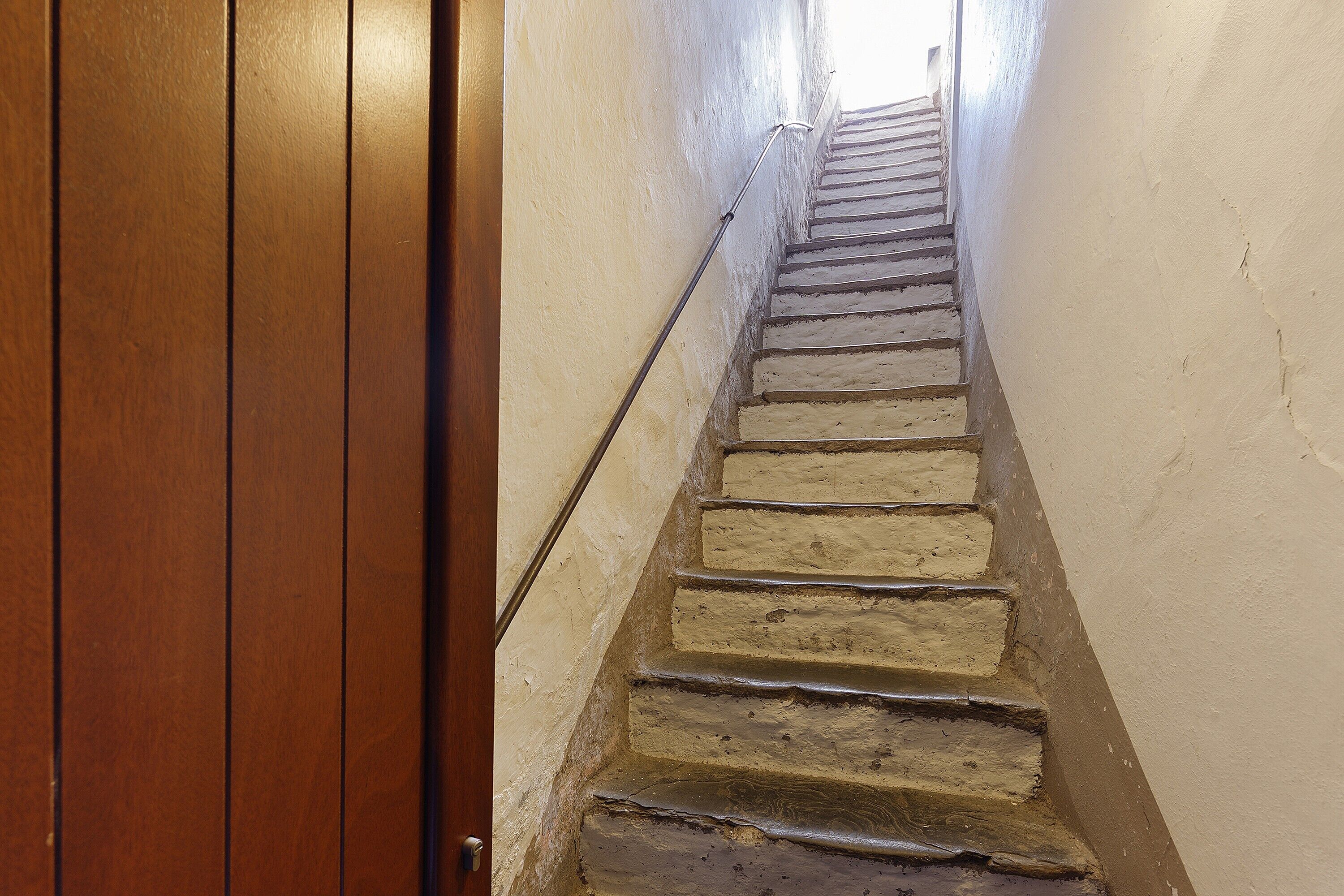 Eine Holztür führt zu einer Wendeltreppe mit Steinstufen und einer Handläufe.