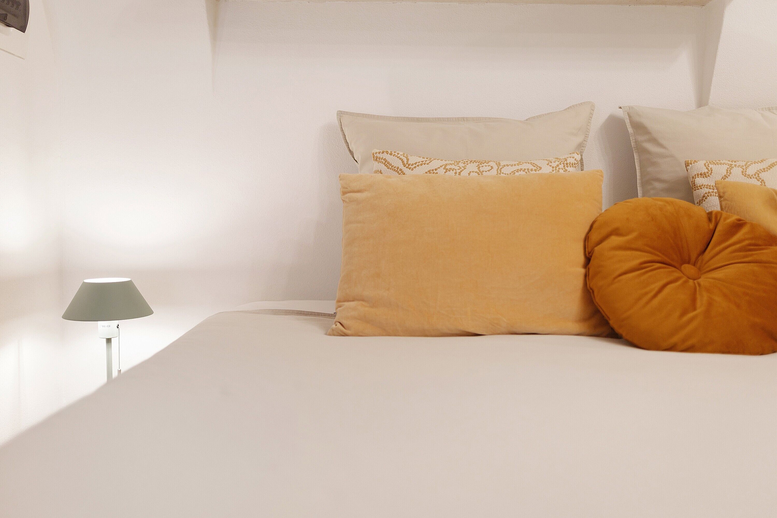 Ein Bett mit weißer Bettwäsche, einer Lampe und zwei Kissen mit Muster.