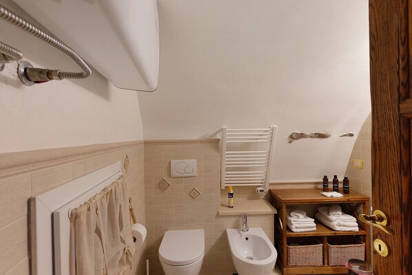 A bathroom with a toilet, bidet, towel rack, and a shelf with toiletries.