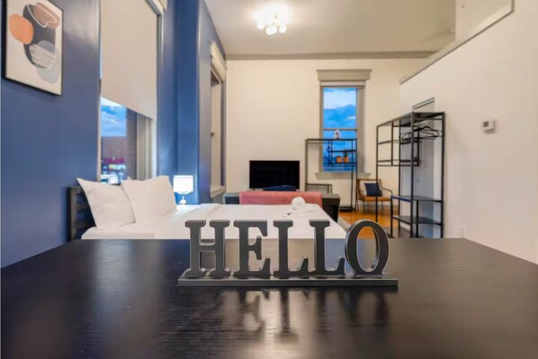 Ein modernes Hotelzimmer mit einem Bett, einem Schreibtisch mit der Aufschrift 'HELLO', einem Fernseher und einem Fenster mit Blick.