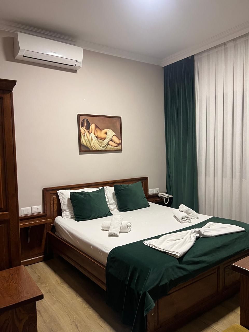 Une chambre d’hôtel avec un lit, un tableau au mur, un climatiseur, un téléphone et une fenêtre avec des rideaux.