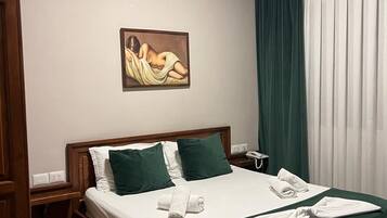 Une chambre d’hôtel avec un lit, un tableau au mur, un climatiseur, un téléphone et une fenêtre avec des rideaux.
