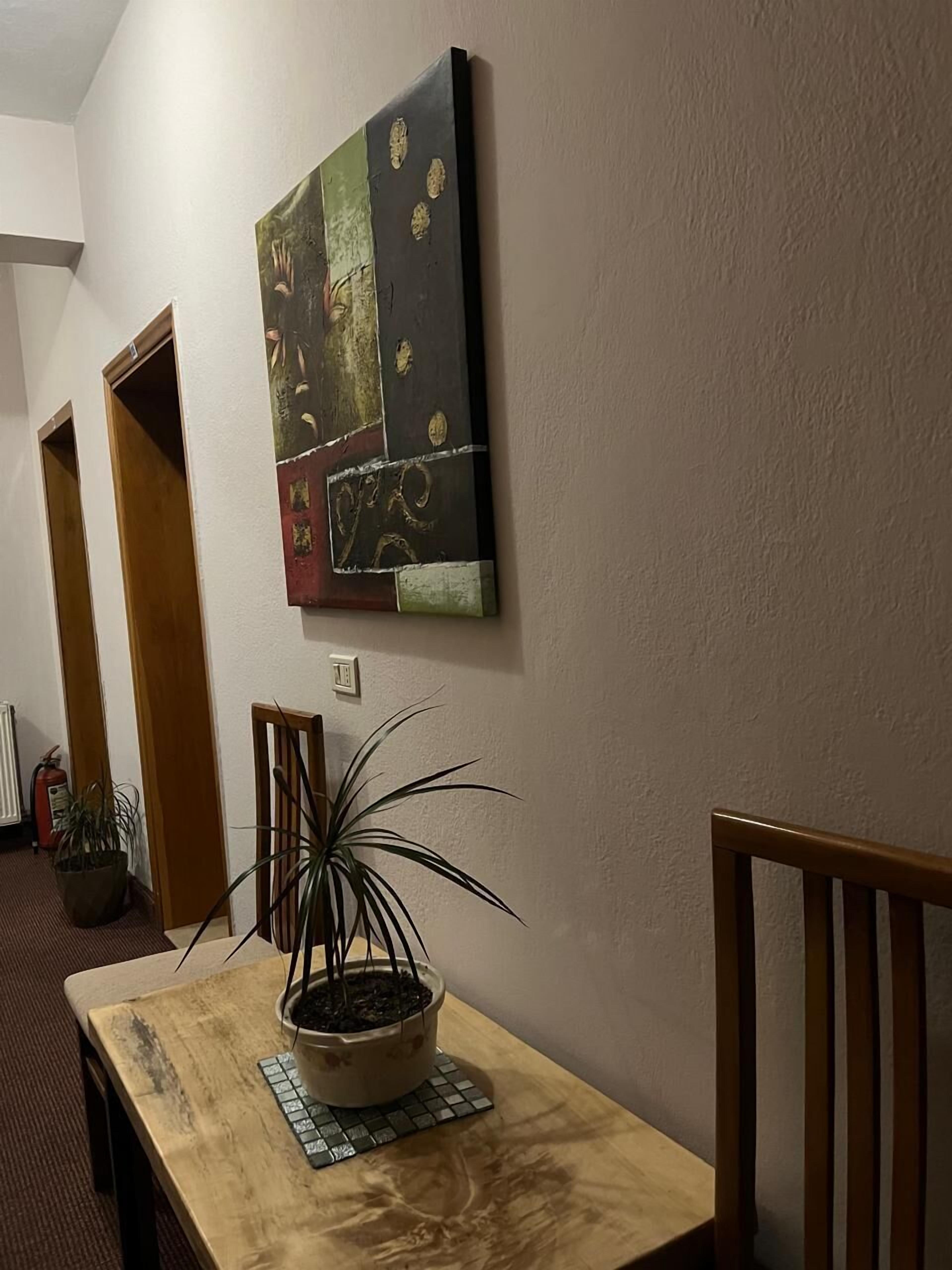 En gang med en træbænk, en potteplante og et billedværk på væggen.