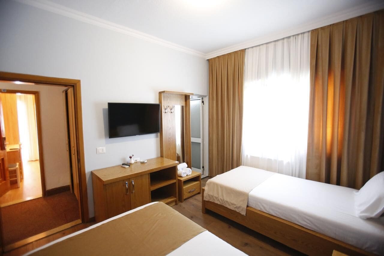A hotel room with a bed, a desk, a TV, a mirror, and a wardrobe.