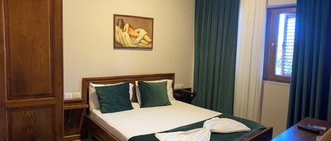 Quarto de hotel com cama de madeira, cortinas verdes, um quadro na parede e uma janela com cortinas.