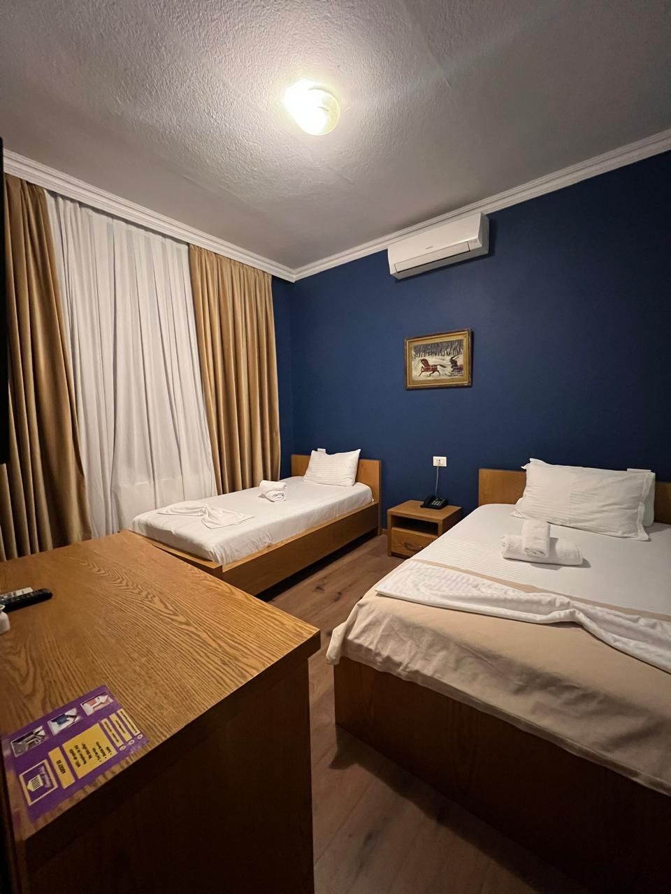 A hotel room with two beds, a desk, a nightstand, and a ceiling light.