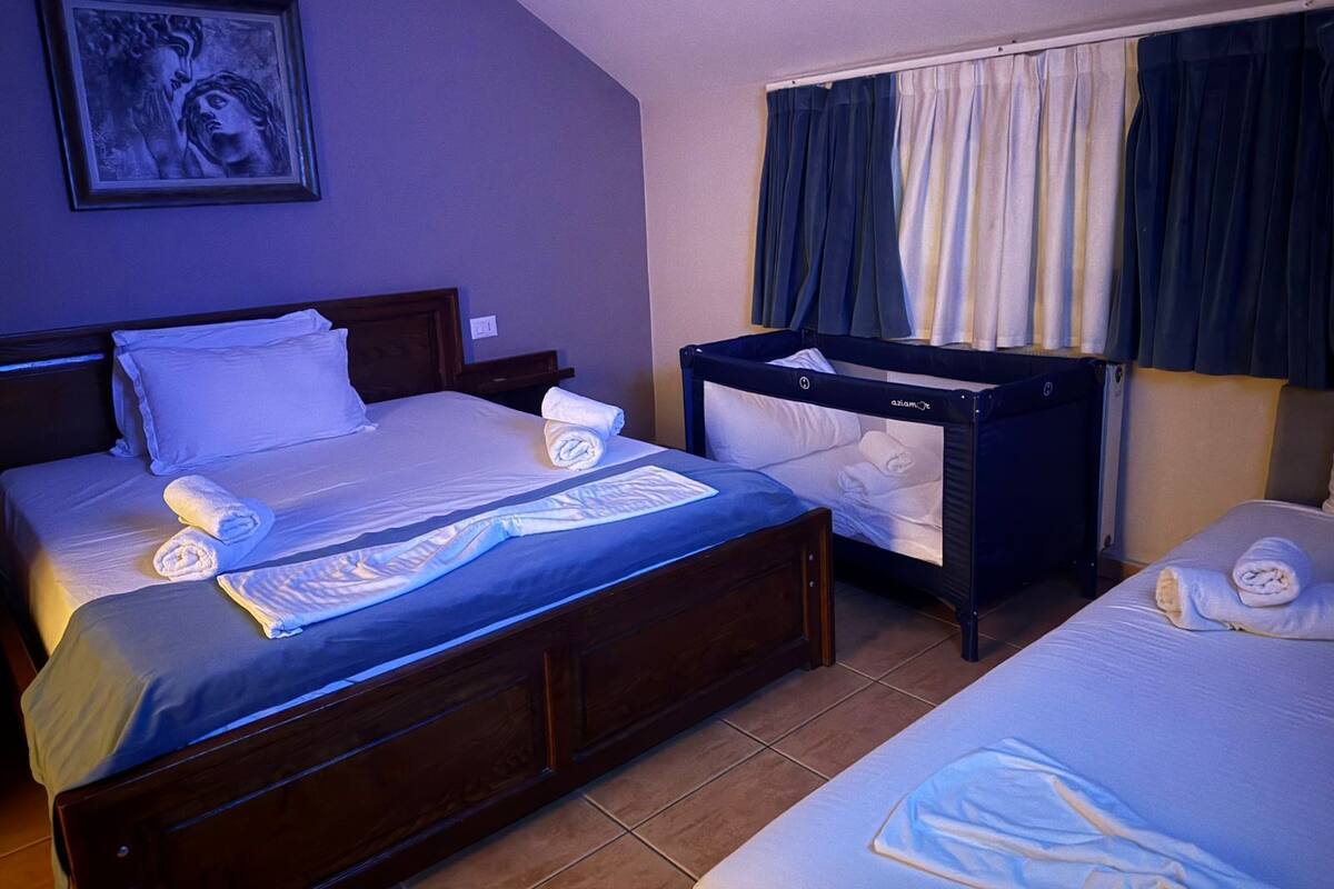 A hotel room with two beds, a crib, and a painting on the wall.
