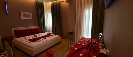 A hotel room with a bed, a small table with a red tablecloth, and a TV mounted on the wall.
