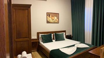 Ein Hotelzimmer mit einem hölzernen Bett, grüner Bettwäsche, einem Bild an der Wand, einer Klimaanlage und einem Fenster mit Vorhängen.