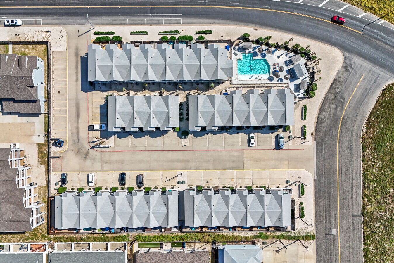 An aerial view of a parking lot with multiple rows of cars, a swimming pool, and a curved road nearby.
