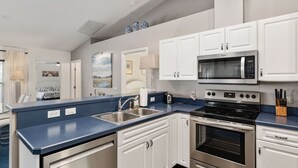 Een moderne keuken met witte kasten, een blauw aanrecht, een magnetron, een fornuis en een spoelbak.