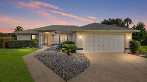 Een gelijkvloers huis met garage, een verzorgd gazon en een aangelegde voortuin met een palmboom.