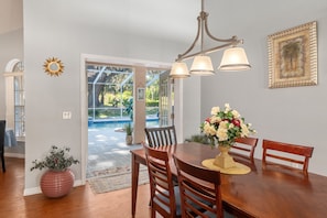 A dining area with a wooden table, chairs, a chandelier, and a view of a swimming pool. - Villa Pearl: 4-bedroom Rental Close To Ocala (Inverness)