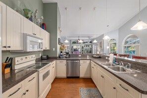 A modern kitchen with white cabinets, granite countertops, stainless steel appliances, and a view of the outdoors through large windows. - Villa Pearl: 4-bedroom Rental Close To Ocala (Inverness)