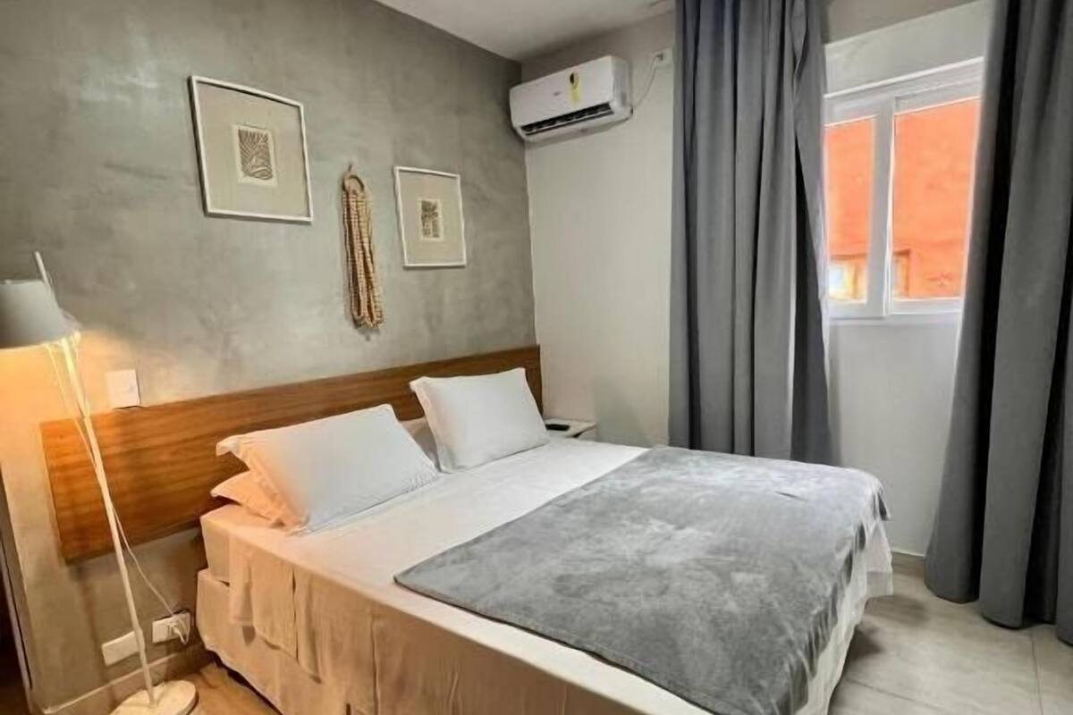 Une chambre à coucher avec un lit, une lampe de chevet, un appareil de climatisation et une fenêtre avec des rideaux.