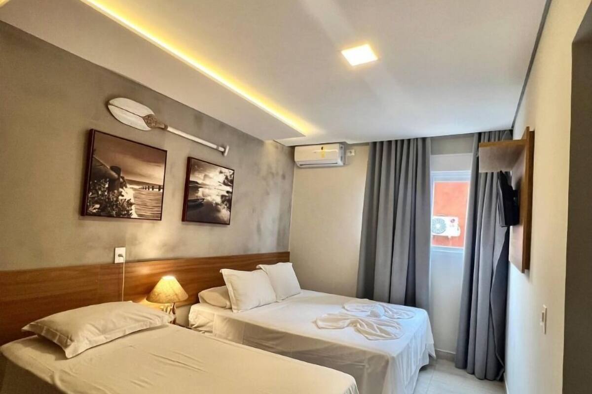 Une chambre d’hôtel avec deux lits, un luminaire au plafond, un climatiseur et un téléviseur fixé au mur.