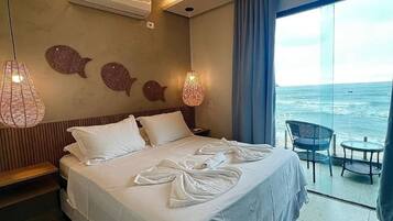Habitación de hotel con una cama grande, un balcón con vistas al mar, una lámpara colgante y un aire acondicionado de pared.