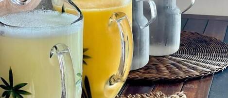 A wooden table with three glass pitchers of orange juice, a metal mug, and a woven placemat.