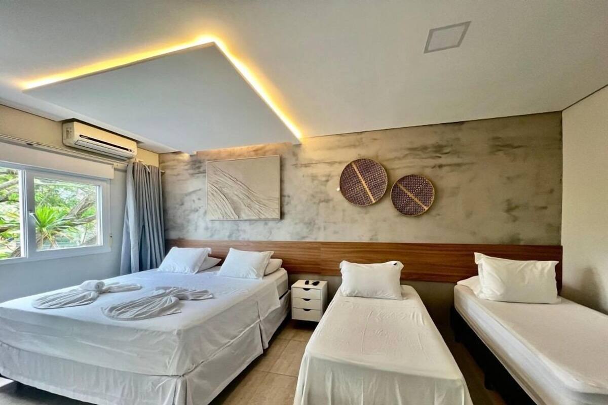 Une chambre d’hôtel comprenant un lit, deux tables de chevet, une commode, une fenêtre avec des rideaux et un mur orné de deux éléments décoratifs en tissu.