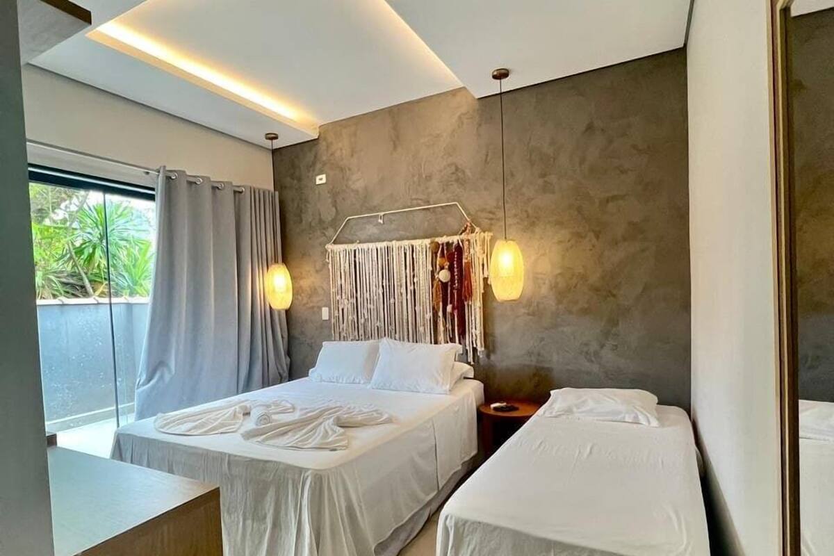Une chambre d’hôtel moderne avec un grand lit, un lit plus petit, un bureau et une vue sur la verdure environnante.