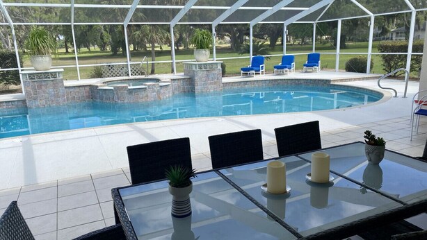 Un espace piscine extérieur avec une table et des chaises en verre, entouré d’une terrasse couverte.