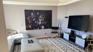 Un salon moderne avec un grand tableau, un canapé, un pouf, un téléviseur et un tapis à motifs.