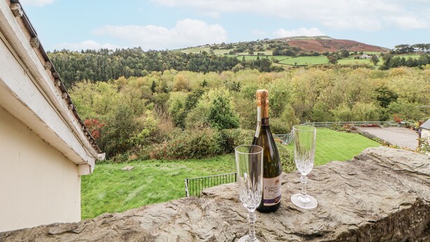 A bottle of wine and two glasses on a stone ledge with a view of a green landscape and hills. - The Hayloft (Abergele)