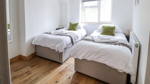A bedroom with two beds, a window, and a hanging light fixture. - The Hayloft (Abergele)
